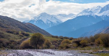 Karla kaplı dağların manzarası. Sonbahar manzarası. Güzel bulutları ve gökyüzü olan küçük bir nehir manzarası. Vahşi doğanın güzelliği.