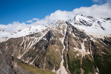 Summer landscape of a mountain peak with the remains of snow on the peaks. A stream of melted ice runs between the mountain slopes.
