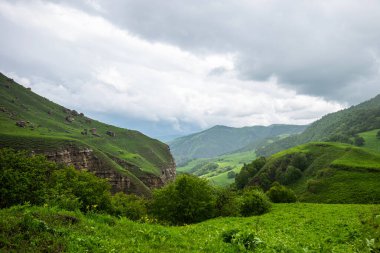 Amazing view of green mountains with clouds and dramatic sky. Majestic mountains and a beautiful green valley surrounded by forested mountains on a rainy spring day.