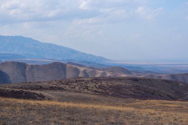 Unusual mountain landscape on a dull autumn day. Remote foothill areas in northern China. Dry grassy fields and hills. Natural background. Exploration of new places, travel to remote locations.