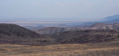 Unusual mountain landscape on a dull autumn day. Remote foothill areas in northern China. Dry grassy fields and hills. Natural background. Exploration of new places, travel to remote locations.
