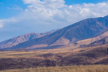 Unusual mountain landscape with bright cloudy skies. Autumn in remote foothills in northern China. Dry grassy and hills. Natural background. Exploration of new places, travel to remote locations.