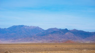 Rocky desert landscape with sparse vegetation and mountains peaks in a blue haze. Typical landscape near at Nepal Tibet border. Flat dry desert with mountains.