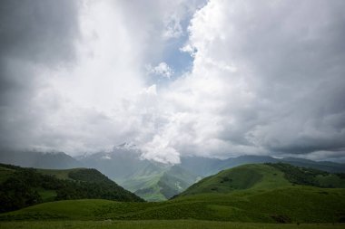 Summer mountain landscape. Amazing view of the valley and lush green pastures in the Caucasus, Georgia. Surrounded by high mountain ranges. Cloudy and rainy day in spring, low storm clouds.