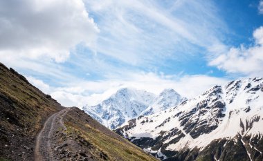 Karda güzel dağ zirveleri. Yüksek dağlı manzara, bulutlu mavi gökyüzü. Doğa. Karanlık bir manzara. Sonbahar platosunun üstündeki parlak, beyaz, karlı zirveler. Dağlarda sonbahar.