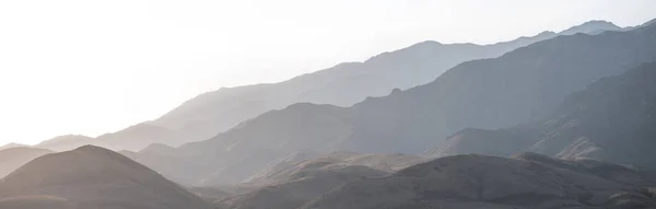 stock image A mountain range with visible silhouettes through the morning fog.