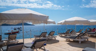 Güzel bir tatil manzarası. Lüks plaj tatil köyü oteli, şemsiyelerin altında güneşli mavi gökyüzü. Sahilde yaz tatili, tatil geçmişi..