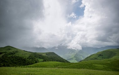 Summer mountain landscape. Amazing view of the valley and lush green pastures in the Caucasus, Georgia. Surrounded by high mountain ranges. Cloudy and rainy day in spring, low storm clouds.