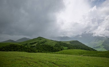Summer mountain landscape. Amazing view of the valley and lush green pastures in the Caucasus, Georgia. Surrounded by high mountain ranges. Cloudy and rainy day in spring, low storm clouds.