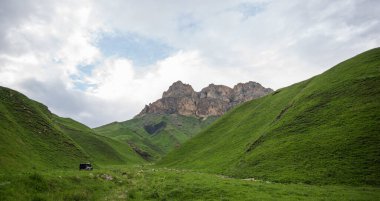 Summer mountain landscape. Amazing view of the valley and lush green pastures in the Caucasus, Georgia. Surrounded by high mountain ranges. Cloudy and rainy day in spring, low storm clouds.
