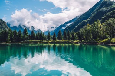 Yaz, gün ışığında dağları yeşil gölün sakin sularına yansıtır. Dağ manzarası, göl ve dağ sırası, geniş bir manzara..