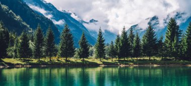 Yaz, gün ışığında dağları yeşil gölün sakin sularına yansıtır. Dağ manzarası, göl ve dağ sırası, geniş bir manzara..