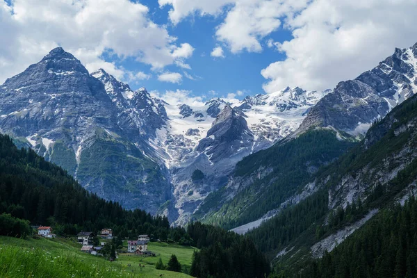 Landscape of the Alps. Snow-capped mountain peaks and beautiful meadows. Freedom, tourism, travel. Peaks on a background of white clouds and blue sky. Green hills and dense forests on the slopes.