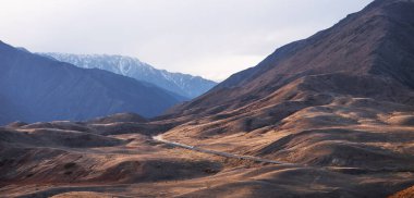 Ufukta mavi bir sisle dağlara doğru sonbahar tepelerinden geçen uzun, dolambaçlı bir yol..