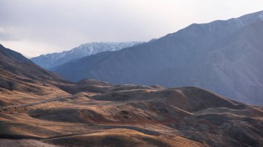 Ufukta mavi bir sisle dağlara doğru sonbahar tepelerinden geçen uzun, dolambaçlı bir yol..