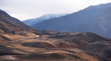 Ufukta mavi bir sisle dağlara doğru sonbahar tepelerinden geçen uzun, dolambaçlı bir yol..
