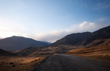 Ufukta mavi bir sisle dağlara doğru sonbahar tepelerinden geçen uzun, dolambaçlı bir yol..