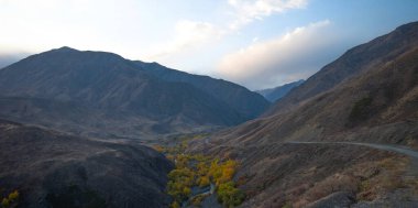 Çin 'in Tibet Özerk Bölgesi' ndeki Tsetan kasabası yakınlarındaki Tibet Platosu 'nda çöl yolu. Gün batımında dağlardan geçen köy yolu. Sonbahar.