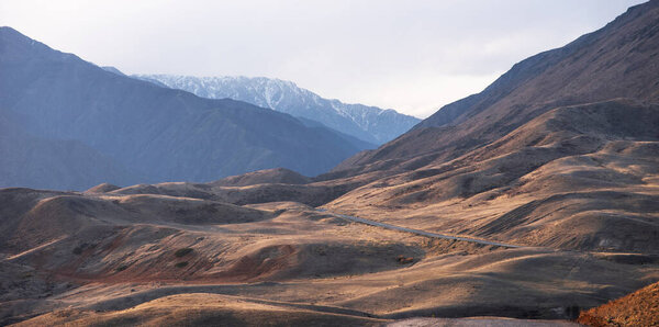 Длинная извилистая дорога через осенние холмы к горам в синей дымке на горизонте.
