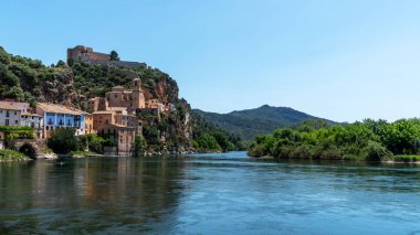 Gök kubbesinin altında görkemli bir kale tarafından taçlandırılmış yemyeşil bir yamaçta yuva yapmış terracotta çatılı evleri olan Idyllic nehir kenarı köyü..