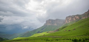 İlkbaharda bulutlu ve yağmurlu bir gün, düşük fırtına bulutları. Dağ manzarası. Gürcistan, Kafkasya 'daki vadi manzarası ve yemyeşil otlaklar inanılmaz. Vadi yüksek sıradağlarla çevrili..