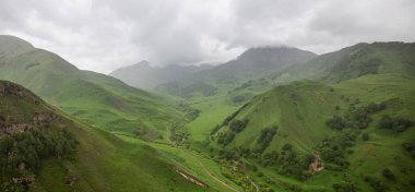 İlkbaharda bulutlu ve yağmurlu bir gün, düşük fırtına bulutları. Dağ manzarası. Gürcistan, Kafkasya 'daki vadi manzarası ve yemyeşil otlaklar inanılmaz. Vadi yüksek sıradağlarla çevrili..