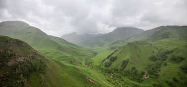 İlkbaharda bulutlu ve yağmurlu bir gün, düşük fırtına bulutları. Dağ manzarası. Gürcistan, Kafkasya 'daki vadi manzarası ve yemyeşil otlaklar inanılmaz. Vadi yüksek sıradağlarla çevrili..