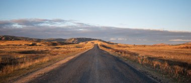 Boş bir kır yolunda gün doğumu muhteşem bir tepenin içinden geçiyor. Sonbaharda renkli çimenli ve tepelik doğal manzara. İç Moğolistan, Çin 'de güzel bir sonbahar manzarası.