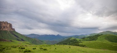 İlkbaharda bulutlu ve yağmurlu bir gün, düşük fırtına bulutları. Dağ manzarası. Gürcistan, Kafkasya 'daki vadi manzarası ve yemyeşil otlaklar inanılmaz. Vadi yüksek sıradağlarla çevrili..