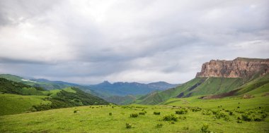 İlkbaharda bulutlu ve yağmurlu bir gün, düşük fırtına bulutları. Dağ manzarası. Gürcistan, Kafkasya 'daki vadi manzarası ve yemyeşil otlaklar inanılmaz. Vadi yüksek sıradağlarla çevrili..