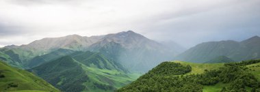 İlkbaharda bulutlu ve yağmurlu bir gün, düşük fırtına bulutları. Dağ manzarası. Gürcistan, Kafkasya 'daki vadi manzarası ve yemyeşil otlaklar inanılmaz. Vadi yüksek sıradağlarla çevrili..