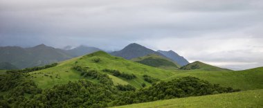 İlkbaharda bulutlu ve yağmurlu bir gün, düşük fırtına bulutları. Dağ manzarası. Gürcistan, Kafkasya 'daki vadi manzarası ve yemyeşil otlaklar inanılmaz. Vadi yüksek sıradağlarla çevrili..