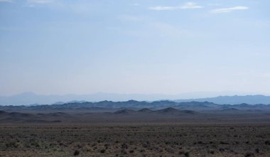 a vast desert landscape under a clear sky with layered mountain silhouettes receding into the distance, creating a serene and expansive view