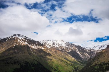 Mountain bright landscape with snow-capped mountain peaks in the distance. Blue sky with fluffy clouds.