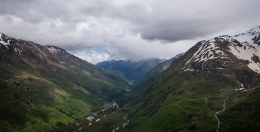 Mountain bright landscape with snow-capped mountain peaks in the distance. Blue sky with fluffy clouds.