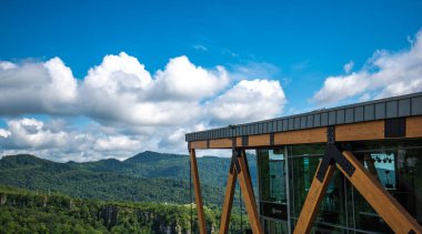 Ahşap kirişler ve camlarla modern bir gözlem platformunun yapısı ziyaretçilere geniş bir gökyüzü altında tüylü beyaz bulutlarla panoramik bir manzara sunuyor.