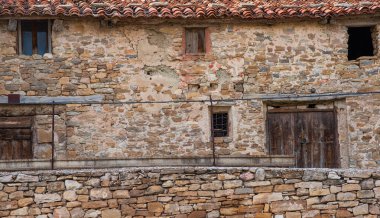Terracotta döşeli çatısı olan eski bir taş binanın dokulu cephesi. Çeşitli taşlardan yapılmış duvarlarda aşınma ve onarım izleri var..