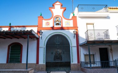 Geleneksel seramik süslerle süslenmiş çarpıcı kırmızı ve beyaz bir cepheli canlı bir İspanyol şapeli ve açık mavi gökyüzüne karşı kurulmuş görünür bir çan.