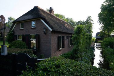 Sazdan çatılı büyüleyici tuğla ev, yemyeşil bir kanalla kaplı dar bir kanalın yanına yerleşmiş, kırsal bir ortamın sükunetini yansıtıyor.