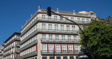 Büyük bir binası olan görkemli bir şehir manzarası. Mimari zarif balkonlar, büyük pencereler ve dekoratif cephelerle karakterize edilir, açık mavi gökyüzünün altında, tarihi bir şehir merkezinde yer alır.