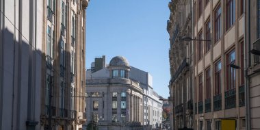 Klasik mimarisi olan bir Avrupa caddesini gözler önüne seren şehir manzarası, berrak mavi gökyüzünün altında kubbeli bir bina merkezi, cephelerde gölge oyunları, sakin, tarihi bir şehrin çeyrek göstergesi..