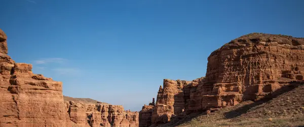 stock image a striking formation of red sandstone cliffs set against a clear azure sky, their rugged textures highlighted by the sunlight, suggesting a peaceful desert scene in daylight