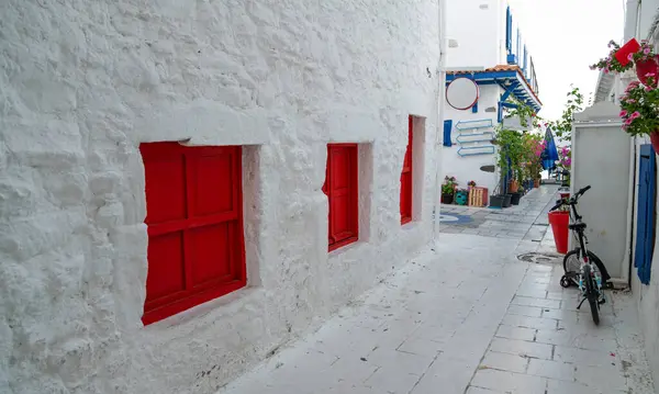stock image a picturesque, narrow alleyway with white walls and striking red shutters, leading to a courtyard with bright flowers and a parked bicycle, reminiscent of a quaint Greek island street.