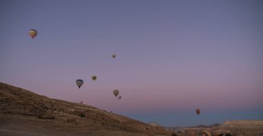 Işıl ışıl sıcak hava balonları, aşağıdaki kurak manzarayla tezat oluşturarak sakin gökyüzüne yükselirler. Günün sonunda sakin ama heyecan verici bir manzara yaratırlar..