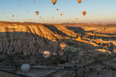 The golden hour casts a warm glow over a breathtaking landscape of unique rock formations, as a multitude of hot air balloons take to the sky in a magical display of flight and color. clipart