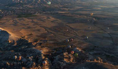 At dawn, hot air balloons float over a sprawling valley shadowed by undulating mountains, their colors vivid against the fading night. Below, patchwork fields and distant towns. clipart