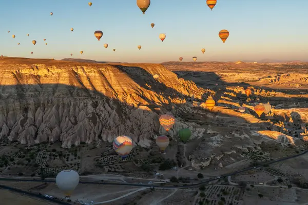 stock image The golden hour casts a warm glow over a breathtaking landscape of unique rock formations, as a multitude of hot air balloons take to the sky in a magical display of flight and color.