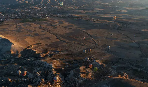 Stock image At dawn, hot air balloons float over a sprawling valley shadowed by undulating mountains, their colors vivid against the fading night. Below, patchwork fields and distant towns.