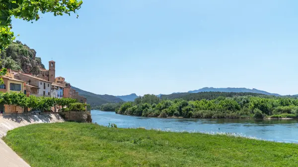 stock image Nestled by a serene river, ancient terracotta-roofed houses bask under a clear sky, framed by verdant hills and the whispers of nature's serenity.