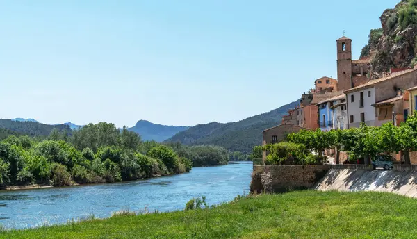 stock image Nestled by a serene river, ancient terracotta-roofed houses bask under a clear sky, framed by verdant hills and the whispers of nature's serenity.